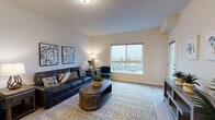 Located at 1403 South Assembly Street in Spokane, WA, Unit B409 is a thoughtfully designed single-floor residence that combines modern finishes with comfortable, functional living. The open-concept layout flows naturally from room to room, finished throughout with light wood-style flooring in the main living areas and plush carpet in the bedroom.

The kitchen is equipped with stainless steel appliances — including a refrigerator, range, and microwave — complemented by rich dark wood cabinetry and light stone countertops, offering ample storage and prep space. Adjacent to the kitchen, the living area is bright and welcoming, featuring a large picture window that frames views of the surrounding neighborhood and treeline, filling the room with natural light.

The bedroom provides a serene retreat, highlighted by a sliding glass door that opens to a private balcony with outdoor views. A dedicated closet with built-in shelving offers practical storage. The unit includes two bathrooms: one featuring a vanity with dark wood cabinetry and a combination tub and shower, and a second full bathroom with a spacious vanity, large mirror, and light-filled layout. A hallway connects the living spaces with clean, neutral-toned walls, creating a cohesive and modern aesthetic throughout.