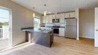 Located at 16 Farmstead Rd in Yarmouth, Maine, this well-appointed single-floor residence offers a clean, modern aesthetic throughout. The open-concept kitchen and living area serves as the heart of the home, featuring light hardwood-style flooring, white shaker cabinetry, granite countertops, and a substantial dark-finished island with pendant lighting overhead. Stainless steel appliances, including a refrigerator, range, and microwave, complete the kitchen. Sliding glass doors lead from the living area to an outdoor deck, allowing an abundance of natural light to fill the space. The living area is equipped with a wall-mounted mini-split heating and cooling system for year-round comfort. The bedrooms are carpeted and bright, each featuring large windows that invite natural light and views of the surrounding greenery, along with individual mini-split units for personalized climate control. The bathrooms are finished with marble-style tile flooring and granite-topped white vanities. One bathroom includes a walk-in shower, while a second features a shower-tub combination. Throughout the residence, neutral wall tones and clean white trim create a cohesive, light-filled atmosphere that lends itself well to a variety of interior styles.