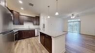 Located on Hadley Blvd in Enola, Pennsylvania, this 1-bedroom, 1-bathroom residence offers a thoughtfully designed single-floor layout with modern finishes throughout. The open-concept kitchen and living area serves as the heart of the home, featuring rich dark-stained cabinetry, granite countertops, and a central island with pendant lighting overhead. Stainless steel appliances, including a refrigerator, range, and built-in microwave, complete the kitchen. Wood-look flooring flows seamlessly through the kitchen and living spaces, adding warmth and continuity. The living room is bright and airy, highlighted by a ceiling fan and a sliding glass door topped with a transom window that opens to a private balcony, inviting abundant natural light and outdoor views. The bedroom offers plush carpeting and connects to a spacious walk-in closet equipped with wire shelving for ample storage. The full bathroom features a tub-shower combo with sleek brushed nickel fixtures, a granite-topped vanity with matching dark cabinetry, and wood-look flooring consistent with the rest of the home. Clean white walls and neutral tones throughout create a bright, move-in-ready atmosphere well-suited for comfortable everyday living.