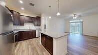 Located on Hadley Blvd in Enola, Pennsylvania, this 1-bedroom, 1-bathroom residence offers a thoughtfully designed single-floor layout with modern finishes throughout. The open-concept kitchen and living area serves as the heart of the home, featuring rich dark-stained cabinetry, granite countertops, and a central island with pendant lighting overhead. Stainless steel appliances, including a refrigerator, range, and built-in microwave, complete the kitchen. Wood-look flooring flows seamlessly through the kitchen and living spaces, adding warmth and continuity. The living room is bright and airy, highlighted by a ceiling fan and a sliding glass door topped with a transom window that opens to a private balcony, inviting abundant natural light and outdoor views. The bedroom offers plush carpeting and connects to a spacious walk-in closet equipped with wire shelving for ample storage. The full bathroom features a tub-shower combo with sleek brushed nickel fixtures, a granite-topped vanity with matching dark cabinetry, and wood-look flooring consistent with the rest of the home. Clean white walls and neutral tones throughout create a bright, move-in-ready atmosphere well-suited for comfortable everyday living.