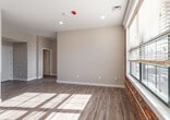 This apartment in Manchester, NH offers a thoughtfully designed single-floor layout combining industrial character with modern updates. The living area serves as the heart of the space, showcasing original exposed brick walls that contrast beautifully with neutral, light-toned painted walls and smooth white baseboards. Large windows flood the room with natural light, casting bright patterns across the light-toned hardwood-style flooring that runs continuously throughout the unit. Recessed lighting provides additional illumination overhead.

The kitchen is well-appointed with white shaker-style cabinetry offering generous storage, granite countertops with a subtle speckled pattern, and a full suite of stainless steel appliances including a gas range, over-the-range microwave, and dishwasher. The layout maximizes efficiency while maintaining an open, clean aesthetic.

Both bedrooms carry the same consistent flooring and neutral wall tones, with natural light entering through windows framed by the building's signature exposed brick. The unit's entry door features a modern keypad lock. Connecting hallways lead seamlessly between rooms, maintaining an open and airy feel throughout this characterful Manchester residence.