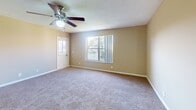This single-floor residence offers a thoughtfully designed layout with a warm, neutral color palette of beige and tan tones carried consistently throughout. The living areas feature plush wall-to-wall carpeting and textured ceilings, creating a comfortable and cohesive atmosphere. Large windows in the main living spaces invite generous natural light and provide views of the surrounding outdoor greenery, while a sliding glass door connects to an outdoor balcony or patio area.

The bedrooms are spacious and carpeted, each equipped with ceiling fans for added comfort. The primary bedroom suite includes direct access to a private en-suite bathroom and a walk-in closet, offering both convenience and storage. A second bedroom similarly connects to a bathroom, maintaining a well-organized layout. The bathrooms feature rich, dark wood vanity cabinetry, light granite-style countertops, hardwood-style flooring, and a shower-tub combination.

The kitchen is outfitted with warm wood cabinetry, a decorative tile backsplash, light stone countertops, and a stainless steel refrigerator. A louvered utility closet provides additional storage or laundry access. Carpeted stairs are also present, suggesting additional access points within the building. Overall, this residence combines functional design with comfortable finishes throughout.