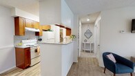 This single-floor residence offers a functional and well-organized layout designed for comfortable everyday living. The kitchen is equipped with warm wood cabinetry, a white electric range, a refrigerator, and a granite-style countertop that extends to form a peninsula, creating a natural division between the kitchen and the adjoining dining area. The dining space accommodates a small bistro-style table and features light wood-look flooring that complements the kitchen's aesthetic.

The living area is carpeted and bright, with a sliding glass door that opens to an outdoor space with views of what appears to be a pool area, allowing for natural light and ventilation. A ceiling-mounted light fixture and textured ceilings are consistent throughout the unit.

The bedrooms are carpeted and finished with neutral-toned walls. One bedroom features a large window with outdoor views and a ceiling fan, while another offers a more intimate feel with warm wall tones. Both rooms provide closet access.

The bathroom includes a wood-toned vanity with a granite-style countertop, a shower-tub combination, and wood-look flooring. A hallway connects the main living spaces, providing a logical and efficient flow throughout the residence.