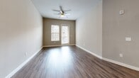 Located at 9600 Gaylord Pkwy in Frisco, TX, this well-appointed one-bedroom, two-bathroom residence offers a thoughtfully designed single-level layout. The open-concept kitchen and living area serves as the heart of the home, featuring rich dark wood cabinetry, granite countertops, a mosaic tile backsplash, stainless steel appliances, and wood-look flooring that flows throughout the main living space. A pendant light over the kitchen island adds a refined touch. The living area extends to a private balcony, offering views of the landscaped courtyard and the multi-story building exterior. The generously sized bedroom is finished with plush carpeting, neutral-toned walls, and a ceiling fan, with natural light entering through large windows. The primary bathroom is well-equipped with a double-sink granite vanity, dark wood cabinetry, a large framed mirror, wood-look tile flooring, and a tiled shower. A walk-in closet with wire shelving is conveniently accessible from the primary bath. The second bathroom provides additional convenience for guests. Neutral gray tones, clean white trim, and consistent finishes throughout lend the space a cohesive, modern aesthetic.
