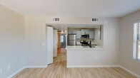This single-floor unit offers a clean, modern layout designed for comfortable everyday living. The open-concept living and dining area is finished with light wood-look flooring and features multiple windows fitted with blinds, filling the space with natural light and providing views of the surrounding greenery. A front entry door with a gold-toned hardware accent adds a welcoming touch.

The kitchen is a standout feature, showcasing a galley-style design with grey two-tone cabinetry, light quartz countertops, and a full suite of stainless steel appliances including a refrigerator, electric range, microwave, and dishwasher. A black matte faucet over a stainless steel sink adds a contemporary contrast. The kitchen opens to the living area via a peninsula counter, creating a connected and functional flow.

The bedrooms are carpeted for comfort, offering a softer feel underfoot. One bedroom includes mirrored sliding closet doors, enhancing the sense of space. The bathroom is bright and practical, featuring light tile-look flooring, a tub-shower combination, and clean white fixtures with matte black hardware accents. Central HVAC vents throughout ensure year-round climate comfort. Overall, the unit presents a cohesive, updated aesthetic with neutral tones throughout.