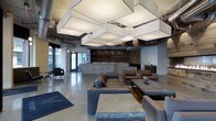 This single-floor space presents a striking industrial-modern aesthetic that blends raw architectural elements with refined, contemporary furnishings. The most distinctive feature overhead is a series of large, square box pendant light fixtures suspended from the ceiling, casting warm, even illumination throughout the open floor plan. Exposed ductwork and heavy wooden beams add an industrial character to the ceiling, contrasting beautifully with the polished concrete floors below.

At the heart of the space sits a substantial reception or bar counter clad in stacked stone, backed by a dramatic reclaimed wood accent wall that adds warmth and texture. The seating area is arranged with generous, low-profile sofas and lounge chairs in neutral tones of gray and brown, accompanied by solid stone-top coffee tables that echo the material palette of the space.

Natural light filters in through large glass doors and windows at the front of the space, offering views to the exterior streetscape. A secondary seating nook near the entrance provides an intimate corner with armchairs for smaller gatherings. The overall ambiance is sophisticated yet approachable, combining the ruggedness of natural stone and reclaimed wood with the sleek finish of polished concrete and modern lighting design.