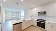 Located at 6461 US-9 N in Howell, NJ, this well-designed one-bedroom, one-bathroom unit offers a thoughtful layout across a single floor. Light wood-tone flooring flows consistently throughout the space, complementing the clean, neutral color palette that creates a bright and airy atmosphere.

The open-concept kitchen is a standout feature, equipped with full stainless steel appliances including a gas range, built-in microwave, dishwasher, and a French-door refrigerator with an ice and water dispenser. White cabinetry with modern hardware lines the walls, accented by a classic white subway tile backsplash and white quartz countertops. Stylish pendant lights hang above the peninsula, which includes an undermount sink and overlooks the adjacent living area — a functional and visually connected layout ideal for everyday living.

The living room is generously proportioned and filled with natural light from large windows fitted with blinds. The bedroom offers a comfortable footprint with a large window providing outdoor views of the surrounding community. A dedicated closet provides practical storage.

The bathroom features light tile flooring, a wide vanity with ample cabinetry, and a clean, minimalist design. A hallway connects the key areas of the unit, maintaining a logical and efficient flow throughout this modern Howell residence.