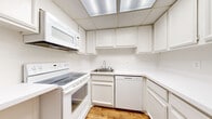 This single-level residence in Southfield, Michigan offers a well-organized layout spanning a generous footprint, accommodating two bedrooms and two full bathrooms. The interior features a consistent, neutral color scheme throughout, with bright white walls and textured ceilings that contribute to a clean, airy atmosphere.

The living area is notably spacious, finished with plush wall-to-wall carpeting and a large window fitted with vertical blinds that allows natural light to filter into the room. A hallway with wood-look flooring connects the main living space to the rest of the unit, providing a clear and functional flow between rooms.

The kitchen is efficiently designed in a U-shaped configuration, featuring white cabinetry, white countertops, and a full suite of white appliances including an electric range, built-in microwave, and dishwasher. Wood-look flooring extends through this area, complementing the bright, uniform cabinetry.

Both bedrooms are carpeted and well-sized, each featuring large windows with vertical blinds and ample closet storage with bifold doors. The bathrooms are finished with white vanities, tile flooring, and large mirrors, maintaining the home's cohesive, clean aesthetic throughout.