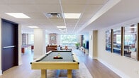 Located at 211 Union St in the heart of Nashville, TN, this well-appointed single-floor commercial space offers a thoughtfully designed layout spanning a generously sized footprint. The interior features light hardwood-style flooring, drop ceilings with recessed panel lighting, and a cohesive neutral palette accented by bold teal feature walls that add character throughout.

The open lounge and entertainment area serves as a central gathering hub, equipped with a pool table, wall-mounted guitar décor, a large flat-screen TV, and comfortable seating — giving the space a relaxed, creative atmosphere. Natural light filters in through windows that frame views of surrounding greenery, enhancing the welcoming ambiance.

A dedicated conference room provides a more formal setting, furnished with a large wooden conference table, upholstered orange chairs, and a wall-mounted display, making it well-suited for meetings and presentations. The kitchen is outfitted with white cabinetry featuring gold hardware, a stainless steel refrigerator, a built-in microwave, and a sink — offering practical convenience for occupants.

A connecting hallway ties the various zones together seamlessly. Throughout the space, dark-stained interior doors provide a striking contrast to the lighter walls and flooring, contributing to a polished, contemporary aesthetic ideal for professional or creative use.