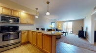 This single-floor residence is designed with an open, flowing layout that connects the kitchen, dining, and living areas into one cohesive space. The kitchen is fully equipped with stainless steel appliances, including a range, built-in microwave, and dishwasher, all complemented by light maple cabinetry and granite countertops. A curved peninsula with bar seating serves as a natural transition point between the kitchen and the rest of the living space, with pendant lighting above adding warm illumination. Tile flooring runs through the kitchen and entry areas, while plush carpet carries through the living and sleeping spaces.

The living room is generously proportioned, featuring large sliding glass doors that open to a private balcony, allowing natural light to fill the space and providing outdoor views. The bedroom is a well-sized, carpeted retreat with ample natural light from a window with blinds and enough room for substantial furniture. The bathroom features a granite-topped vanity with maple cabinetry, tile flooring, and a combined tub and shower. Throughout the unit, neutral warm tones create a cohesive and comfortable atmosphere.