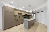 This contemporary apartment showcases a thoughtful design that maximizes space and functionality. The heart of the home is an impressive open-concept kitchen, featuring light wood cabinetry, stainless steel appliances, and a large central island with pendant lighting. The kitchen seamlessly flows into a spacious living area, characterized by light wood-look flooring that runs throughout the entire space, creating a cohesive and airy atmosphere.

Large windows and glass doors provide ample natural light and offer views of the surroundings. The living spaces are versatile, with room for dining and relaxation. A bedroom area is evident, offering privacy and comfort. The bathroom is modern and minimalist, with clean lines and a neutral color palette.

Storage solutions are integrated throughout, including a walk-in closet with built-in shelving. The apartment's design emphasizes clean lines, neutral tones, and a bright, open feel. Recessed lighting and contemporary fixtures add to the modern aesthetic. This well-designed space offers a perfect blend of style and functionality for comfortable urban living.