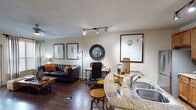 Located at 7510 Burgoyne Rd in Houston, TX, this single-floor residence offers a thoughtfully designed open-concept layout that seamlessly connects the main living areas. The living room is a standout space, featuring rich dark hardwood flooring, crown molding, and large windows fitted with blinds and draping curtains that invite natural light while maintaining privacy. A tufted leather sofa anchors the sitting area, complemented by track lighting overhead.

The kitchen is well-equipped and centrally positioned, showcasing warm honey-toned cabinetry, granite countertops, and a curved breakfast bar with seating for two. Stainless steel appliances — including a refrigerator, range, microwave, and dishwasher — provide a full suite of modern conveniences.

The bedroom is a comfortable retreat with a ceiling fan, natural light from double windows, and ample space for furnishings. The full bathroom continues the granite countertop theme, paired with warm wood cabinetry, tile flooring, and a full tub-shower combination with tile surround.

Throughout the residence, neutral warm tones create a cohesive and inviting ambiance, while consistent hardwood-style flooring in the main areas ties the space together with a sense of continuity and understated elegance.