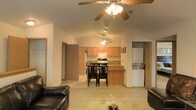This single-floor space is defined by its open-concept layout, which seamlessly connects the living room, dining area, and kitchen into one cohesive and functional environment. Vaulted ceilings rise overhead, enhancing the sense of volume and airiness throughout the main living area. Ceiling fans are installed in both the living and kitchen zones, providing both comfort and a casual aesthetic.

The living room is furnished with leather seating and centers around a coffee table, offering a relaxed and comfortable gathering space. Adjacent to it, a dining area accommodates a dark wood table and chair set, positioned conveniently between the living room and kitchen.

The kitchen features warm honey-toned wood cabinetry, a gas range, and a peninsula counter that doubles as additional prep and dining space. A refrigerator and range hood complete the functional cooking area, keeping the layout practical and efficient.

A dedicated laundry alcove is tucked to the side, housing a stacked washer and dryer unit — a convenient in-unit feature. Additional doorways lead to other areas of the home, suggesting further private rooms beyond the open main living zone. Light-toned flooring runs throughout, tying the spaces together with a clean and consistent finish.