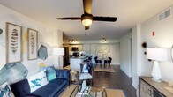 This single-floor residence offers a thoughtfully designed open-concept layout that seamlessly connects the living, dining, and kitchen areas. The living room features dark hardwood-style flooring, a ceiling fan with light fixture, and a sliding glass door that opens to a private balcony with outdoor views, allowing natural light to fill the space. Decorative accent walls add visual interest throughout.

The kitchen is well-equipped with stainless steel appliances, including a refrigerator, range, and microwave. Dark granite countertops extend along an oversized island with bar seating, complemented by light cabinetry, a subway tile backsplash, and track lighting overhead. A dedicated dining area sits adjacent to the kitchen.

The bedrooms are carpeted and generously sized, each featuring ceiling fans and large windows. The primary bedroom includes a sliding glass door providing direct balcony access and views of the surrounding landscape. Additional bedrooms offer ample natural light.

Both bathrooms are finished with white subway tile tub-shower combinations, white tile flooring, and dark granite vanity countertops, presenting a clean and functional aesthetic throughout.