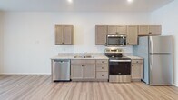 Located at 609 W 86th St in Sioux Falls, South Dakota, this single-floor unit offers a clean, modern design with a practical and efficient layout. Light wood-tone flooring runs throughout the space, creating a warm and cohesive aesthetic.

The kitchen is a standout feature, outfitted with a full suite of stainless steel appliances including a refrigerator, electric range with over-the-range microwave, and dishwasher. Taupe shaker-style cabinetry provides ample storage, while granite-look countertops add a refined touch. Recessed lighting illuminates the space from above.

The living area is bright and open, benefiting from large windows dressed with vertical blinds that allow natural light to filter through. A wall-mounted PTAC unit provides individualized climate control. The open layout seamlessly connects the living and kitchen areas, contributing to an airy, uncluttered feel.

The bathroom is thoughtfully finished with a granite-topped vanity, an undermount sink, and a walk-in shower with clean white surrounds and a chrome showerhead. Wood-toned cabinetry and doors echo the design language found throughout the unit.

Overall, the space presents a fresh, contemporary interior with consistent finishes, making it a functional and inviting environment.