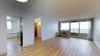 This 2-bedroom, 1.5-bathroom residence offers a well-organized single-floor layout designed for comfortable urban living. The open living area is immediately welcoming, featuring light-toned hardwood-style flooring that runs throughout the space, creating a clean and cohesive aesthetic. Large floor-to-ceiling windows flood the living room with natural light and provide sweeping city views, giving the unit an airy, elevated feel. A wall-mounted climate control unit ensures year-round comfort. The living area flows naturally toward a hallway that connects the bedrooms and bathrooms, maintaining a logical and efficient floor plan. The kitchen is accessible from the main living space and features cabinetry that provides ample storage. The 1.5-bathroom configuration includes a full bath and a convenient half bath, adding practicality for residents and guests alike. Crisp white walls throughout the unit enhance the brightness brought in by the generous window line. The overall ambiance is clean, modern, and move-in ready, making this a highly functional residence that balances open communal areas with private sleeping quarters in a compact yet thoughtfully designed footprint.
