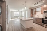 This single-floor residence at 901 River Rd in Charlottesville, Virginia offers a thoughtfully designed layout with modern finishes throughout. The kitchen is a standout feature, showcasing rich walnut-toned cabinetry extending from floor to ceiling, sleek white countertops, and a classic white subway tile backsplash. A full suite of stainless steel appliances — including a refrigerator with ice maker, electric range, built-in microwave, and dishwasher — provides everything needed for everyday cooking. Light wood-tone flooring runs throughout the main living areas, lending warmth and continuity to the space. Adjacent to the kitchen, the dining area comfortably accommodates a table and chairs, flowing naturally into the living room. The living room is bright and airy, benefiting from multiple windows that invite natural light and feature white horizontal blinds. A ceiling fan adds to the comfort of the space. The bedroom is carpeted for comfort and includes a large window with exterior views. The full bathroom is clean and functional, featuring a tub-shower combination with white tile surround, a wood-toned vanity with white countertop, and light wood flooring. Overall, the unit presents a contemporary aesthetic with a neutral palette, offering a comfortable and well-appointed living environment in Charlottesville.