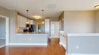 Located at 3115 Orchard Vista Dr SE in Grand Rapids, Michigan, this single-floor home offers a well-designed layout with a cohesive neutral color palette throughout. The open-concept living and kitchen area serves as the heart of the home, where warm hardwood-style flooring flows seamlessly across the space. Large windows in the living area allow generous natural light to fill the room, enhancing the airy, welcoming ambiance.

The kitchen is thoughtfully equipped with crisp white cabinetry, a tile backsplash, gray countertops, and stainless steel appliances including a gas range, over-the-range microwave, and refrigerator. A central island with pendant lighting overhead provides additional prep space and casual seating. An adjacent dining area features a classic chandelier and a glass-panel door leading to an outdoor balcony.

The bedrooms are finished with soft neutral walls and plush carpeting, offering a comfortable and quiet retreat. Two bathrooms serve the home — one featuring a walk-in shower with white cabinetry and wood-tone flooring, and another with a full soaking tub and similar finishes. The consistent use of white trim, warm tones, and practical finishes throughout gives the home a clean, move-in-ready character.