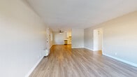 This single-story home is thoughtfully laid out across a compact footprint, accommodating three bedrooms, one bathroom, a combined kitchen and living area, and a connecting hallway. Light hardwood-style flooring runs consistently throughout the entire home, lending a cohesive and clean aesthetic to every room.

The open living area is bright and welcoming, featuring neutral beige walls, white baseboards, and a ceiling fan. Large windows allow natural light to fill the space while providing outdoor views of surrounding greenery. The living area flows directly into the kitchen, which stands out with white shaker-style cabinetry, white quartz countertops, a stainless steel sink, and a full suite of stainless steel appliances including a refrigerator, gas range with over-the-range microwave, and dishwasher.

The three bedrooms are modest in scale, each featuring the same hardwood-style flooring and neutral wall tones. The primary bedroom receives ample natural light and includes closet space with a hanging rod. The single bathroom is finished with white tile surrounding a shower-tub combination, dark slate floor tiles, and a window for ventilation and natural light.