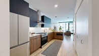 Located at 218 E Grand Ave in Chicago's vibrant Streeterville neighborhood, this thoughtfully designed one-bedroom, one-bathroom residence offers a sleek, contemporary living experience across a single floor. The open-concept kitchen and living area forms the heart of the home, showcasing a striking two-tone kitchen with bold navy upper cabinetry, warm walnut-finish lower cabinets, white subway tile backsplash, light stone countertops, and stainless steel appliances including a gas range with a stainless steel hood. Light hardwood flooring runs throughout, lending a sense of warmth and continuity. The living area is anchored by floor-to-ceiling windows and a glass-panel door that opens onto a private balcony, filling the space with abundant natural light and offering sweeping views of the Chicago skyline and surrounding architecture. The bedroom is a cozy, well-appointed retreat featuring clean white walls, floating wood wall shelves, and continued hardwood flooring. The bathroom features grey tile flooring, a wood-accented vanity, and crisp white walls with matte black hardware accents. A dedicated entrance and thoughtful layout round out this efficient yet stylish urban residence.