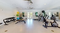 Located in Daphne, Alabama, this fitness center offers a well-organized and comprehensively equipped exercise facility designed to support a wide range of workout routines. The space features light-toned large-format tile flooring throughout, crisp white walls accented with crown molding, and recessed lighting complemented by ceiling fans that ensure comfortable air circulation during workouts.

Natural light fills the room through multiple windows and a set of glass French doors, which also provide views of the surrounding greenery and easy access to the outdoors. Full-length wall mirrors on one side of the room enhance the sense of space and allow users to monitor their form during exercise.

The cardio zone is well-stocked with treadmills, an elliptical trainer, and a stationary bike, while wall-mounted flat-screen televisions keep users entertained. The strength training area includes a multi-station cable machine, an adjustable weight bench, and a full dumbbell rack. A dedicated functional fitness corner houses a storage rack stocked with stability balls in various sizes, resistance bands, medicine balls, and exercise mats, catering to flexibility and core training needs. The layout is spacious and thoughtfully arranged, providing ample room to move freely between equipment stations.