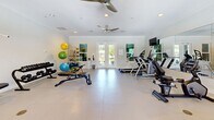 Located in Daphne, Alabama, this fitness center offers a well-organized and comprehensively equipped exercise facility designed to support a wide range of workout routines. The space features light-toned large-format tile flooring throughout, crisp white walls accented with crown molding, and recessed lighting complemented by ceiling fans that ensure comfortable air circulation during workouts.

Natural light fills the room through multiple windows and a set of glass French doors, which also provide views of the surrounding greenery and easy access to the outdoors. Full-length wall mirrors on one side of the room enhance the sense of space and allow users to monitor their form during exercise.

The cardio zone is well-stocked with treadmills, an elliptical trainer, and a stationary bike, while wall-mounted flat-screen televisions keep users entertained. The strength training area includes a multi-station cable machine, an adjustable weight bench, and a full dumbbell rack. A dedicated functional fitness corner houses a storage rack stocked with stability balls in various sizes, resistance bands, medicine balls, and exercise mats, catering to flexibility and core training needs. The layout is spacious and thoughtfully arranged, providing ample room to move freely between equipment stations.