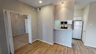 Located at 17717 Vail St in Dallas, Texas, this single-floor unit offers a clean, modern aesthetic with a well-designed open-concept layout. The living area is bright and welcoming, featuring wood-look flooring, neutral gray walls, and a ceiling fan with light fixture. Natural light flows in through multiple windows fitted with blinds, and a sliding glass door opens to an outdoor view of surrounding greenery, adding a refreshing sense of connection to the exterior.

The kitchen is efficiently designed with a peninsula-style breakfast bar topped with granite-look countertops, white cabinetry, and a full suite of stainless steel appliances including a refrigerator, range, and over-the-range microwave. The kitchen opens directly to the living and dining areas, making the space feel cohesive and functional.

A hallway leads to additional rooms, including a carpeted area visible through a doorway, suggesting a bedroom with a softer flooring finish. The bathroom is neatly appointed with a granite-topped vanity, wood-look flooring, a tiled shower-tub combination, and brushed nickel fixtures throughout. The textured ceilings add a subtle architectural detail consistent across the unit. Overall, the space presents a tidy, move-in-ready environment with contemporary finishes.