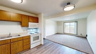 This 2-bedroom, 1-bathroom unit in Sioux Falls, South Dakota, offers a practical and well-organized single-floor layout. The kitchen serves as the entry point to the living area and features warm-toned wood cabinetry, a double-basin sink, and white appliances including a refrigerator, dishwasher, electric range, and microwave. Durable wood-look vinyl flooring runs throughout the kitchen, while plush carpet covers the living areas and bedrooms. The open living room is generously proportioned, filled with natural light from a sliding glass door that leads to a private balcony with outdoor views. A wall-mounted mini-split unit provides additional climate control alongside baseboard heating found throughout the unit. Both bedrooms are comfortably sized with carpeted floors, natural light from windows with blinds, and views of the surrounding area. The primary bedroom features two sliding closet doors, offering ample storage. The full bathroom includes a single-sink vanity with wood cabinetry, a toilet, and a tub-shower combination. Textured ceilings and warm wood trim carry consistently throughout the space, giving the unit a cohesive, understated aesthetic. An electrical panel is accessible within the unit for added convenience.