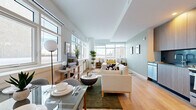Located at 50 Clinton Street in New Rochelle, NY, this thoughtfully designed studio offers a contemporary open-plan layout that maximizes every square foot. Light hardwood flooring runs throughout, lending warmth and visual continuity to the entire space.

The combined kitchen and living area forms the heart of the unit. The kitchen is outfitted with flat-front wood-toned cabinetry, a dark tile backsplash, stainless steel appliances including a full-size refrigerator, gas range, microwave, and dishwasher, and a sleek sink — all arranged along a single efficient wall. The living area flows seamlessly from the kitchen, benefiting from large windows on multiple walls that allow abundant natural light and views of the surrounding neighborhood.

The bathroom features a clean, modern aesthetic with a walk-in glass-enclosed shower finished in white subway tile, gray geometric floor tiling, brushed nickel fixtures, and a floating wood-tone vanity with a white countertop and integrated sink.

A dedicated walk-in closet provides organized storage with adjustable shelving and hanging rods. The sleeping area accommodates a full-size bed and is further enhanced by a bank of oversized windows that frame open exterior views, creating a bright, airy retreat. Soft sage-toned walls complement the light-filled interiors throughout.