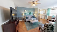Located at 650 W Flintlake Ct in Myrtle Beach, SC, this single-floor home offers a cohesive coastal-inspired design throughout. The open-concept living and dining area is bright and welcoming, featuring warm hardwood-style flooring, large windows dressed with vibrant teal curtains that allow generous natural light, and a ceiling fan overhead. The living area flows seamlessly into the dining space, which is anchored by a pendant light fixture and surrounded by additional windows for an airy feel.

The kitchen is practical and well-equipped, offering ample cabinetry with wood-toned upper cabinets and white lower cabinets, a double sink, dishwasher, electric range, and a full-size refrigerator. A window above the sink adds natural light to the workspace.

The home includes multiple bedrooms, each distinctly styled with bold accent walls — one features a rich teal wall paired with soft carpet and direct access to a bathroom, while another showcases a striking navy accent wall with a teal upholstered headboard and seating area. Both rooms provide a restful, design-forward atmosphere.

The bathrooms are clean and functional, each featuring a tub-shower combination, wood-look flooring, a single vanity with a wide mirror, and stylish curtain accents. A dedicated laundry area with full-size washer and dryer connections rounds out this well-planned home.