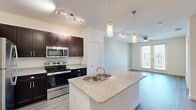Located at 2808 E McKinney St in Denton, TX, this one-bedroom, one-bathroom unit offers a well-designed single-floor layout with a cohesive modern aesthetic throughout. The open-concept kitchen serves as the centerpiece of the living space, featuring rich dark cabinetry, granite countertops, a spacious center island with an integrated sink, and a full suite of stainless steel appliances including a range, microwave, and refrigerator. Elegant pendant lighting above the island adds a polished touch, while a track lighting system provides ample task illumination. Light wood-look plank flooring runs consistently throughout the unit, contributing to a clean, contemporary feel. The living area flows naturally from the kitchen and is brightened by large sliding glass doors that invite natural light and provide outdoor access. A ceiling fan is present in both the living area and the bedroom, enhancing comfort year-round. The bedroom is a comfortably sized retreat with a dedicated window overlooking the exterior and includes access to a closet. The bathroom is well-appointed with a tiled tub-shower combo, a dark vanity with granite countertop, and wood-look flooring that ties the space together seamlessly.