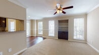 This single-story residence offers a well-organized layout designed for comfortable everyday living. The living area is a standout space, featuring warm neutral-toned walls, crown molding, and a ceiling fan with a light fixture overhead. A textured ceiling adds subtle architectural detail, while multiple windows fitted with blinds fill the room with natural light and offer outdoor views. The flooring transitions from rich hardwood near the entryway to plush carpeting throughout the main living and bedroom areas. A built-in shelving unit with dark cabinetry provides both display and storage space along one wall, enhancing the room's functionality.

The galley-style kitchen is efficiently arranged, with dark espresso cabinetry lining both sides, hardwood flooring, and white appliances including a refrigerator, range, and microwave. The entryway area features a half-wall partition that defines the transition between spaces, along with a closet and ceiling fan.

The bedrooms are carpeted and bright, each featuring crown molding, ceiling fans, and large windows. Closet space is included in the bedrooms. The bathroom is clean and straightforward, with a full tub and shower combination surrounded by classic white square tile.