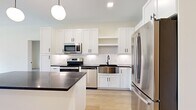 This well-appointed single-floor residence offers 2 bedrooms, 2 bathrooms, and two closets, thoughtfully designed with modern finishes throughout. Light hardwood flooring flows consistently across the entire space, creating a cohesive and airy feel.

The kitchen is a standout feature, showcasing crisp white shaker-style cabinetry extending to the ceiling, dark countertops, a stainless steel farmhouse sink, and a full suite of stainless steel appliances including a range, microwave, dishwasher, and French door refrigerator. A central island with a dark countertop provides additional prep space and casual seating, while a globe pendant light adds a modern accent.

The living room is bright and open, anchored by large floor-to-ceiling sliding glass doors with rich wood-toned frames that lead to a private balcony overlooking a green outdoor area.

The primary bedroom is generously proportioned, featuring its own set of sliding glass doors to the balcony and a large walk-in closet with wire shelving. The second bedroom offers a sizable window with outdoor views.

Both bathrooms are finished in a clean, contemporary style. One features white shaker vanity cabinetry, dark countertops, matte black fixtures, a large rectangular mirror, and a sliding glass shower-tub enclosure.