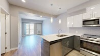 Located at 3265 Glen Drive in Vancouver's Mount Pleasant neighbourhood, this modern 2-bedroom, 2-bathroom unit offers a thoughtfully designed layout with clean, contemporary finishes throughout. Light hardwood flooring flows seamlessly across the open-plan living and kitchen area, creating a warm and cohesive aesthetic. The kitchen is outfitted with light wood cabinetry, white lower cabinets, stainless steel appliances including a built-in oven and refrigerator, and a subtle tile backsplash — combining functionality with modern style. The living area is bright and welcoming, featuring a large window framing treetop and neighbourhood views, complemented by open shelving and a neutral colour palette. Both bedrooms are serene and well-lit, each with large windows that invite natural light and offer elevated views of the surrounding Vancouver landscape. The primary bedroom includes a dedicated closet. Two bathrooms serve the unit: one features a glass-enclosed walk-in shower with wood-toned vanity cabinetry, while the second offers a full soaker tub with large-format tile surround. A generous outdoor terrace provides sweeping mountain and treetop views under open skies, ideal for relaxing or entertaining. The hallway connects all rooms efficiently with clean white panelled doors and modern hardware throughout.