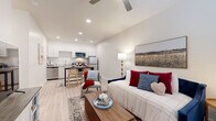 Located at 5900 N 99th Ave in Phoenix, Arizona, this thoughtfully designed studio unit offers an efficient single-floor layout that maximizes every square foot. The open-concept living and kitchen area creates a seamless flow throughout the space, anchored by light-toned luxury vinyl plank flooring that runs consistently across all rooms.

The kitchen is fully equipped with stainless steel appliances, including a refrigerator, electric range, over-the-range microwave, and dishwasher. Crisp white cabinetry provides ample storage, while a compact dining table with seating for two serves as a functional centerpiece between the kitchen and living areas. Recessed lighting illuminates the kitchen, keeping the space bright and welcoming.

The living area features a ceiling fan, a wall-mounted mini-split HVAC unit for climate control, and a window with blinds and patterned curtains that allow for natural light. The neutral white walls throughout create a clean, airy ambiance.

A hallway leads to the full bathroom, which includes a tub-shower combination with built-in shelving, a toilet, and a vanity, all finished in crisp white tones that complement the light flooring. The unit's straightforward layout and modern finishes make it a practical and comfortable living space.