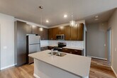 Located at 1316 Big Bend Rd in Twin Oaks, MO, this well-appointed two-bedroom, two-bathroom residence offers a thoughtfully designed single-floor layout. The modern kitchen is a standout feature, showcasing rich dark-wood cabinetry, a mosaic tile backsplash, stainless steel appliances including a refrigerator, range, and built-in microwave, and a central island with a double-basin sink and pendant lighting overhead. Light wood-style flooring flows throughout the main living and kitchen areas, creating a warm, cohesive aesthetic. The spacious living room features a ceiling fan and connects seamlessly to the rest of the home. The generously sized primary bedroom includes a large walk-in closet outfitted with wire shelving for ample storage. Both bedrooms are carpeted and filled with natural light from well-positioned windows. The bathrooms feature dark cabinetry vanities with light countertops and wood-look flooring. A dedicated in-unit laundry room houses a full-size front-loading washer and dryer with overhead wire shelving. The overall design is clean and contemporary, with neutral tones and modern finishes throughout.