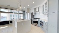 Located at 300 E Main St, this single-floor space offers a thoughtfully designed, open-concept layout with a clean, contemporary aesthetic throughout. The kitchen serves as a true centerpiece, showcasing a large quartz-topped island with an undermount sink and elegant globe pendant lighting overhead. Cabinetry is finished in a two-tone palette — crisp white uppers with soft sage-blue lowers — complemented by white subway tile backsplash and light porcelain tile flooring. Professional-grade stainless steel appliances, including a multi-burner range with a stainless hood and a French door refrigerator, cater to serious culinary pursuits. Glass-front upper cabinets add a refined, airy touch. Floor-to-ceiling windows flood the kitchen and adjoining living areas with abundant natural light, framing striking urban skyline views that enhance the sense of openness and scale. The seamless flow between spaces creates an inviting environment well-suited for both everyday living and entertaining. The overall ambiance is bright, modern, and sophisticated, with high-end finishes and thoughtful details that elevate the space throughout.
