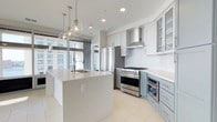Located at 300 E Main St, this single-floor space offers a thoughtfully designed, open-concept layout with a clean, contemporary aesthetic throughout. The kitchen serves as a true centerpiece, showcasing a large quartz-topped island with an undermount sink and elegant globe pendant lighting overhead. Cabinetry is finished in a two-tone palette — crisp white uppers with soft sage-blue lowers — complemented by white subway tile backsplash and light porcelain tile flooring. Professional-grade stainless steel appliances, including a multi-burner range with a stainless hood and a French door refrigerator, cater to serious culinary pursuits. Glass-front upper cabinets add a refined, airy touch. Floor-to-ceiling windows flood the kitchen and adjoining living areas with abundant natural light, framing striking urban skyline views that enhance the sense of openness and scale. The seamless flow between spaces creates an inviting environment well-suited for both everyday living and entertaining. The overall ambiance is bright, modern, and sophisticated, with high-end finishes and thoughtful details that elevate the space throughout.