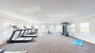 Located at 1740 Willow St in Faribault, Minnesota, this fitness center offers a well-equipped, single-floor exercise space designed to support a wide range of workout routines. The room features a clean, modern aesthetic with white walls, a smooth white ceiling lined with recessed lighting, and durable patterned carpet flooring throughout.

Natural light fills the space through multiple large windows along the walls, providing views of the surrounding area and creating a bright, energizing atmosphere. The cardio section is well-stocked with two treadmills and an elliptical machine, all positioned to take advantage of the natural light from the windows. At the center of the room stands a full multi-station cable machine, ideal for a comprehensive strength training regimen, complemented by a set of dumbbells and a yoga mat for floor exercises. A dedicated area along one wall houses a rack of medicine balls and stability balls in various sizes, catering to functional fitness and balance training.

A wall-mounted flat-screen TV adds an entertainment element to the space, and a table suitable for ping-pong or utility use is also present. The room is generously proportioned, offering ample open floor space between equipment to ensure comfortable movement throughout. A wall-mounted HVAC unit provides climate control, ensuring year-round usability of the facility.