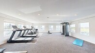 Located at 1740 Willow St in Faribault, Minnesota, this fitness center offers a well-equipped, single-floor exercise space designed to support a wide range of workout routines. The room features a clean, modern aesthetic with white walls, a smooth white ceiling lined with recessed lighting, and durable patterned carpet flooring throughout.

Natural light fills the space through multiple large windows along the walls, providing views of the surrounding area and creating a bright, energizing atmosphere. The cardio section is well-stocked with two treadmills and an elliptical machine, all positioned to take advantage of the natural light from the windows. At the center of the room stands a full multi-station cable machine, ideal for a comprehensive strength training regimen, complemented by a set of dumbbells and a yoga mat for floor exercises. A dedicated area along one wall houses a rack of medicine balls and stability balls in various sizes, catering to functional fitness and balance training.

A wall-mounted flat-screen TV adds an entertainment element to the space, and a table suitable for ping-pong or utility use is also present. The room is generously proportioned, offering ample open floor space between equipment to ensure comfortable movement throughout. A wall-mounted HVAC unit provides climate control, ensuring year-round usability of the facility.