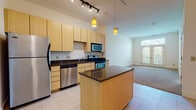 Located at 4437 Glengarry Dr in Beavercreek, Ohio, this single-floor residence offers a thoughtfully designed open-concept layout that seamlessly integrates the kitchen and living areas. The kitchen is a standout feature, showcasing light maple cabinetry that extends to impressive heights, dark granite countertops, and a full suite of stainless steel appliances including a refrigerator, electric range, microwave, and dishwasher. A central island with matching granite provides additional prep space and casual seating potential. Stylish pendant lighting in warm amber tones and a track lighting system illuminate the space from above, highlighting the soaring ceiling height that adds a sense of openness throughout. Large-format tile flooring runs through the kitchen and entry areas, while plush neutral carpeting defines the open living space, which benefits from natural light streaming through a glass-panel exterior door leading to an outdoor area. The bedrooms feature carpeted floors and generous windows that invite natural light. A clean, functional bathroom with tile flooring includes a full tub/shower combination and a classic white fixture suite. Multiple interior closets, including louvered-door units, provide ample storage throughout the home.
