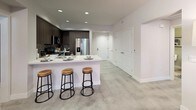 This well-appointed single-floor residence offers a thoughtfully designed open-concept layout that balances contemporary style with everyday functionality. The kitchen is a standout feature, showcasing dark wood cabinetry that reaches to the ceiling, crisp white quartz countertops, stainless steel appliances, a herringbone tile backsplash, and a central island with bar seating — ideal for casual dining and entertaining. The living and dining area is bright and inviting, with large windows that frame outdoor views and flood the space with natural light. The room is anchored by bold abstract artwork and flows seamlessly into a glass-top dining area with a warm wood bookshelf nearby. The primary bedroom is generously sized with a ceiling fan, a walk-in closet, and distinctive decor including a chevron wood headboard. The second bedroom also features a ceiling fan, natural light from a large window, and outdoor views. Both bathrooms are finished with dark wood vanities, white quartz counters, and framed mirrors. The full guest bath includes a tiled soaking tub with shower and built-in shelving. Throughout the space, neutral tones, recessed lighting, and consistent finishes create a cohesive and modern aesthetic.