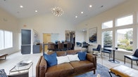 Located at 6060 Rossi Drive in Canal Winchester, Ohio, this single-story home offers a thoughtfully designed open-concept layout that seamlessly blends living, dining, and kitchen areas into one expansive, connected space. The great room commands immediate attention with its soaring vaulted ceilings and a striking sputnik chandelier that serves as a bold focal point, complemented by recessed lighting throughout. Large windows invite abundant natural light, enhancing the airy, welcoming ambiance of the interior. The living area features rich brown leather seating accented with navy blue cushions, anchored by a soft area rug that adds warmth and texture to the light-toned flooring. Adjacent to the living space, a generously sized dining area accommodates a large table surrounded by dark upholstered chairs, ideal for both everyday meals and entertaining. A stylish barn door adds a contemporary architectural detail, separating spaces while maintaining visual flow. The kitchen area is visible in the background, offering a cohesive continuation of the home's modern aesthetic. Tasteful wall art and carefully curated furnishings contribute to the sophisticated, yet comfortable atmosphere that defines this well-appointed Canal Winchester residence.