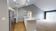 Located at 4430 N Holland Sylvania Rd in Toledo, OH, this 2-bedroom, 2-bathroom residence offers a thoughtfully designed single-floor layout with standout architectural details throughout. Soaring vaulted ceilings define the open-concept living and kitchen area, creating an airy, expansive atmosphere. The kitchen features white cabinetry, a glass-front upper cabinet, stainless steel appliances including a refrigerator and range, a peninsula with an integrated sink and generous counter space, and warm hardwood-style flooring. A charming arched doorway connects the kitchen to the rest of the home, adding a classic architectural touch. Track lighting illuminates the space effectively throughout. Both bedrooms are carpeted and benefit from vaulted ceilings and windows that invite natural light, providing a comfortable, restful environment. The primary bedroom is generously sized and includes a double-door closet. The primary bathroom offers a dual-sink vanity with ample cabinetry and drawer storage, a tub/shower combo, and tile flooring. The second bathroom is clean and functional, also featuring a tub/shower combo and tile flooring. A carpeted hallway with closet access connects the rooms seamlessly, completing this well-appointed and move-in-ready home.