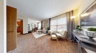 This two-story home offers four bedrooms and two bathrooms thoughtfully distributed across two floors. The main level features a welcoming living room bathed in natural light from large windows dressed with elegant gray curtain panels, offering views of the surrounding neighborhood. Warm, neutral-toned carpeting flows throughout the living and dining areas, creating a cohesive and comfortable atmosphere. A gallery wall of framed artwork adds a polished, curated touch to the living space. The adjacent dining area is positioned near bright windows, making it an inviting spot for everyday meals. The kitchen is outfitted with warm oak cabinetry, dark countertops, and standard appliances including a range, microwave, and refrigerator, all set on easy-care tile flooring. Upstairs, the primary bedroom is generously sized with carpeted floors, a window for natural light, and closet space for storage. Additional bedrooms share the same comfortable carpeted finishes and neutral tones. The bathrooms feature tiled tub-shower combinations with clean, classic finishes. Throughout the home, the neutral color palette, textured ceilings, and consistent flooring choices create a warm, livable environment suited for a range of lifestyles.