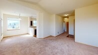 Located at 10520 Creek St SE in Yelm, Washington, unit E-308 is a well-designed single-floor residence that offers a comfortable and functional living environment. The open living area immediately impresses with soaring vaulted ceilings that amplify the sense of space, complemented by soft, neutral-toned carpeting underfoot and warm cream-colored walls throughout. Natural light streams in through multiple windows, creating a bright and welcoming atmosphere across the living spaces.

The layout flows naturally from the spacious living area into a dedicated kitchen space, which features dark cabinetry, countertop workspace, and tile flooring — a practical setup for everyday living. A hallway connects the main living zone to several well-proportioned bedrooms, each finished with plush carpeting, baseboard heating, and windows that frame views of the surrounding neighborhood and tree-lined landscape. The bedrooms offer a quiet, comfortable retreat with ample wall space for furnishings.

The bathroom is cleanly finished with a full soaking tub and shower combination, chrome fixtures, a vanity with sink, and a large mirror. Tile flooring and neutral wall tones give the space a tidy, functional appeal. Throughout the unit, consistent finishes and thoughtful details contribute to a cohesive, move-in-ready residence in the heart of Yelm, WA.