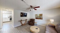 This two-story home offers a well-organized layout with two bedrooms, two bathrooms, and a thoughtful distribution of living space across both floors. The main level hosts the combined kitchen and living area, a hallway, a utility room, and staircase access to the upper floor.

The living room features light wood-style flooring, neutral painted walls, a textured ceiling, and a ceiling fan with a light fixture. A wall-mounted TV, natural light from a leaded glass window, and warm, casual furnishings create a comfortable and inviting atmosphere.

The kitchen is equipped with white cabinetry, light countertops, a stainless steel range, dishwasher, and built-in microwave. A window above the sink allows natural light into the space, complemented by track lighting overhead.

The upper floor contains both bedrooms and two full bathrooms. The spacious primary bedroom features plush carpeting, a ceiling fan, a natural light window with decorative leaded glass, and ample room for a full furniture arrangement. The second bedroom is cozy with carpeted flooring, a ceiling fan, and a window offering natural light. One bathroom features a tub-shower combo with wood-style flooring, while the second bathroom includes a vanity with light countertops. A staircase connects the two floors efficiently.