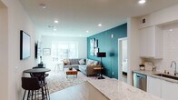 This well-appointed single-floor residence showcases a contemporary open-concept design with a seamless flow between the kitchen, dining, and living areas. The kitchen is a standout feature, equipped with stainless steel appliances, a gas range, a French-door refrigerator, white flat-panel cabinetry, a subway tile backsplash, and an expansive granite island that doubles as a breakfast bar. Recessed lighting and light wood-tone flooring run throughout, creating a bright and cohesive aesthetic. The living room centers around a bold teal accent wall adorned with curated artwork, complemented by large windows that invite natural light and outdoor views. A dedicated dining nook with bar-height seating adds functional versatility to the open layout. The primary bedroom features a soothing sage green accent wall, direct access to an en-suite bathroom with a walk-in glass shower, white cabinetry, and a large vanity mirror. A secondary bedroom offers dual windows with natural light and ample space. A second full bathroom includes a white vanity and tub-shower combination. A cozy reading nook with an accent chair and additional window rounds out the thoughtfully designed interior.