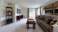 Located at 4604 Owings Mills Road in Owings Mills, Maryland, this single-floor residence offers a thoughtfully designed layout that balances comfort and functionality. The living room is generously proportioned, featuring plush wall-to-wall carpeting, crown molding, and a large sliding glass door that floods the space with natural light and provides views of the surrounding greenery. A wall-mounted flat-screen television and media console anchor one side of the room, while the seating area is oriented to take advantage of the outdoor views.

Adjacent to the living room, the dedicated dining area accommodates a full dining table and connects seamlessly to the kitchen via a pass-through window. The kitchen is outfitted with warm wood cabinetry, granite-style countertops, a coil-element range, and tile flooring, offering ample storage and prep space.

The residence includes two carpeted bedrooms, each featuring closet space and windows that bring in natural light. The primary bedroom is notably spacious, with room for a full bedroom suite. The full bathroom is clean and efficiently appointed, featuring tile flooring, a white vanity, and a shower-tub combination. Crown molding throughout the main living areas adds a refined architectural detail to the overall design.