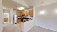 Located in the Broadlands community of Ashburn, VA, this well-appointed 2-bedroom, 1-bathroom home offers a thoughtfully designed single-level layout. The combined kitchen and living area serves as the heart of the home, featuring soaring vaulted ceilings with a pendant light fixture and soft carpet flooring. The living room is bathed in natural light through a glass-paneled entry door and sidelight window, opening to an outdoor deck area. The kitchen is well-equipped with warm honey-toned cabinetry, dark granite countertops, a breakfast bar, and a full suite of stainless steel appliances including a gas range, dishwasher, microwave, and refrigerator, all finished with light tile flooring. The primary bedroom offers generous proportions, crown molding, a ceiling fan, and wide windows overlooking green surroundings. The second bedroom also features large windows and plush carpet, filling the space with natural light. The full bathroom is clean and functional, with white tile flooring and a tub-shower combination. A dedicated laundry area houses a full-size side-by-side washer and dryer with overhead wire shelving for additional storage, adding a convenient everyday amenity to this comfortable home.